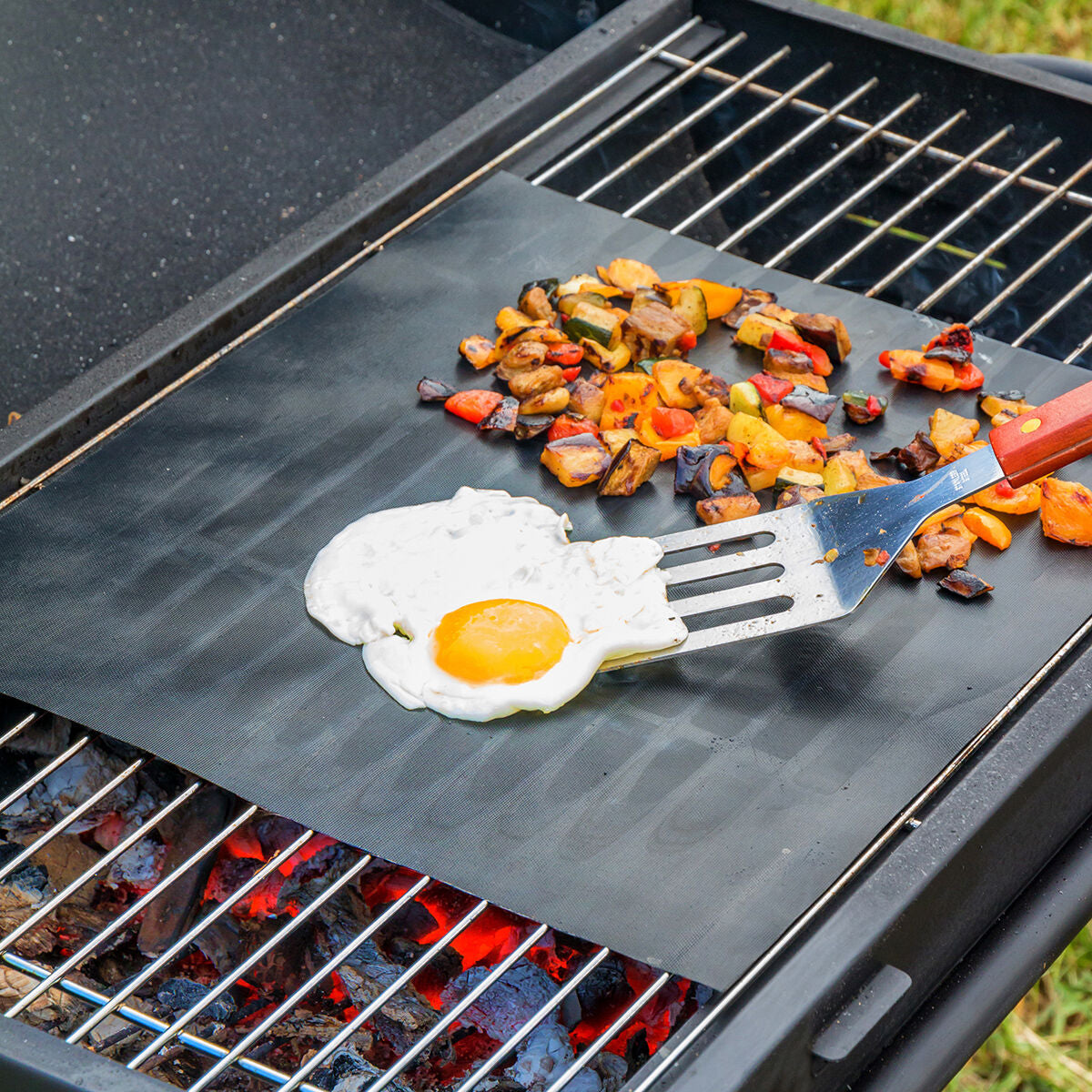 Grillmatte auf einem Rost mit Ei und Gemüse sowie einem Pfannenwender