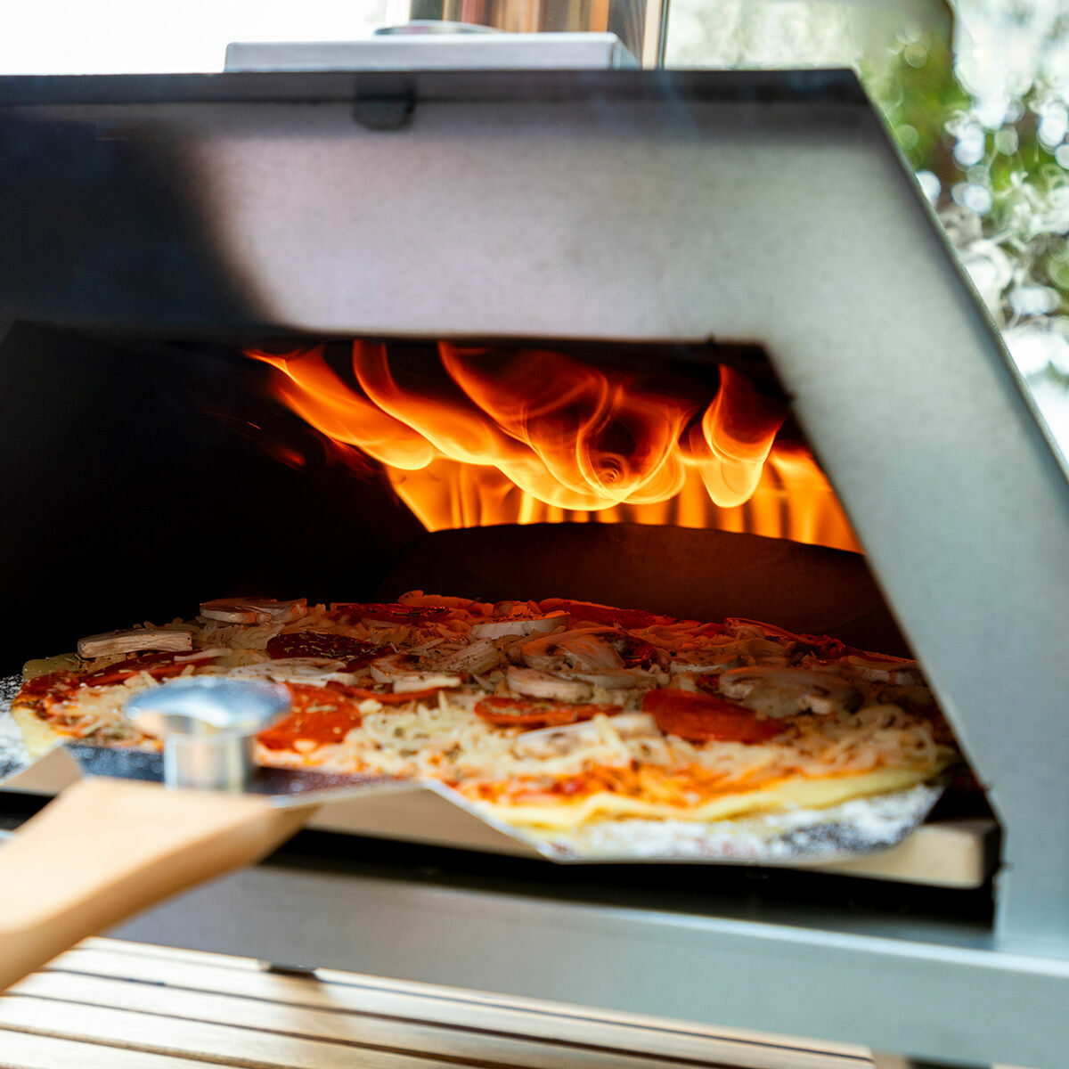 Nahansicht der Pizzahven-Backöffnung mit Pizza auf dem Stein und Flammen im Hintergrund