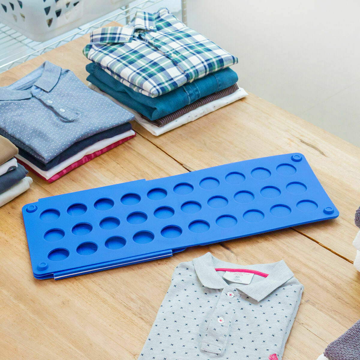 Zusammengeklapptes blaues Wäschefaltbrett neben gefalteter Kleidung