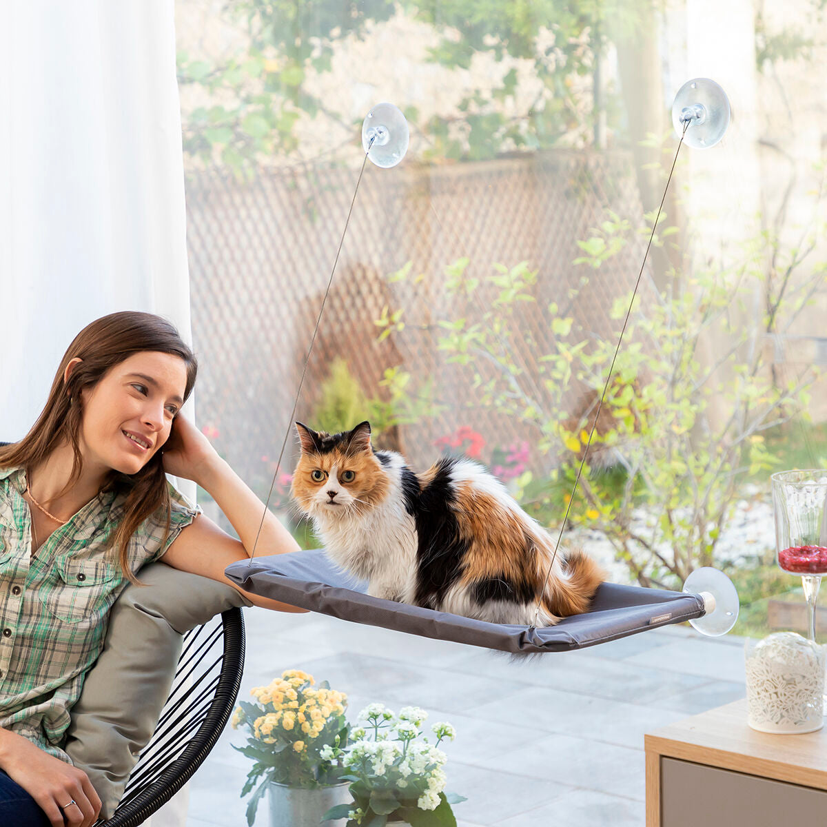 Katze auf der Catlax Fensterliege neben einer sitzenden Frau