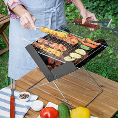 Person grillt Speisen auf dem aufgeklappten Foldecue-Mini-Holzkohlegrill im Freien